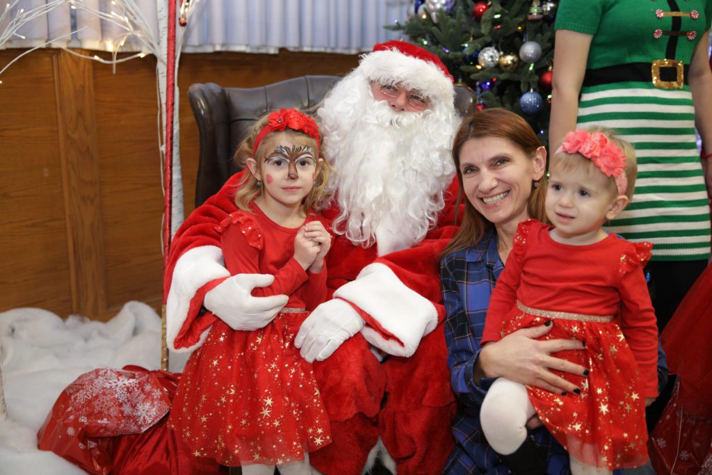 Two children in Christmas outfits with mom and Santa Claus
